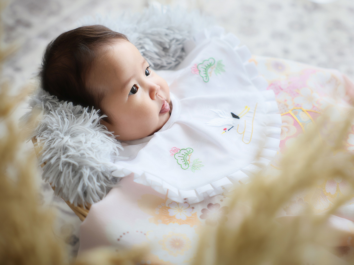 着物の上で横になるスタイ姿の赤ちゃん