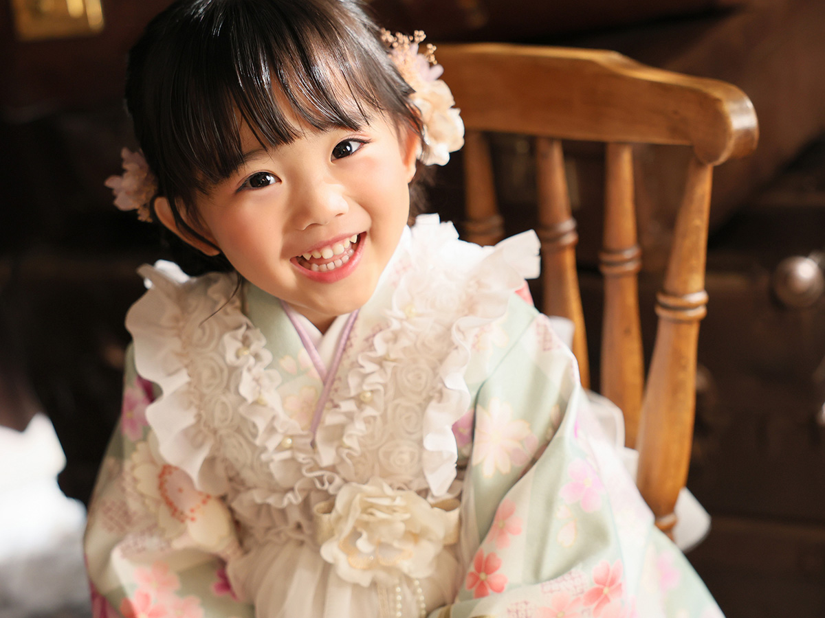 七五三の被布姿で椅子のそばで笑う女の子